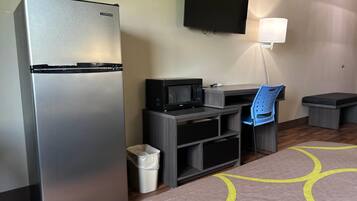Habitación de hotel con refrigerador, microondas, escritorio, silla y televisor montado en la pared.