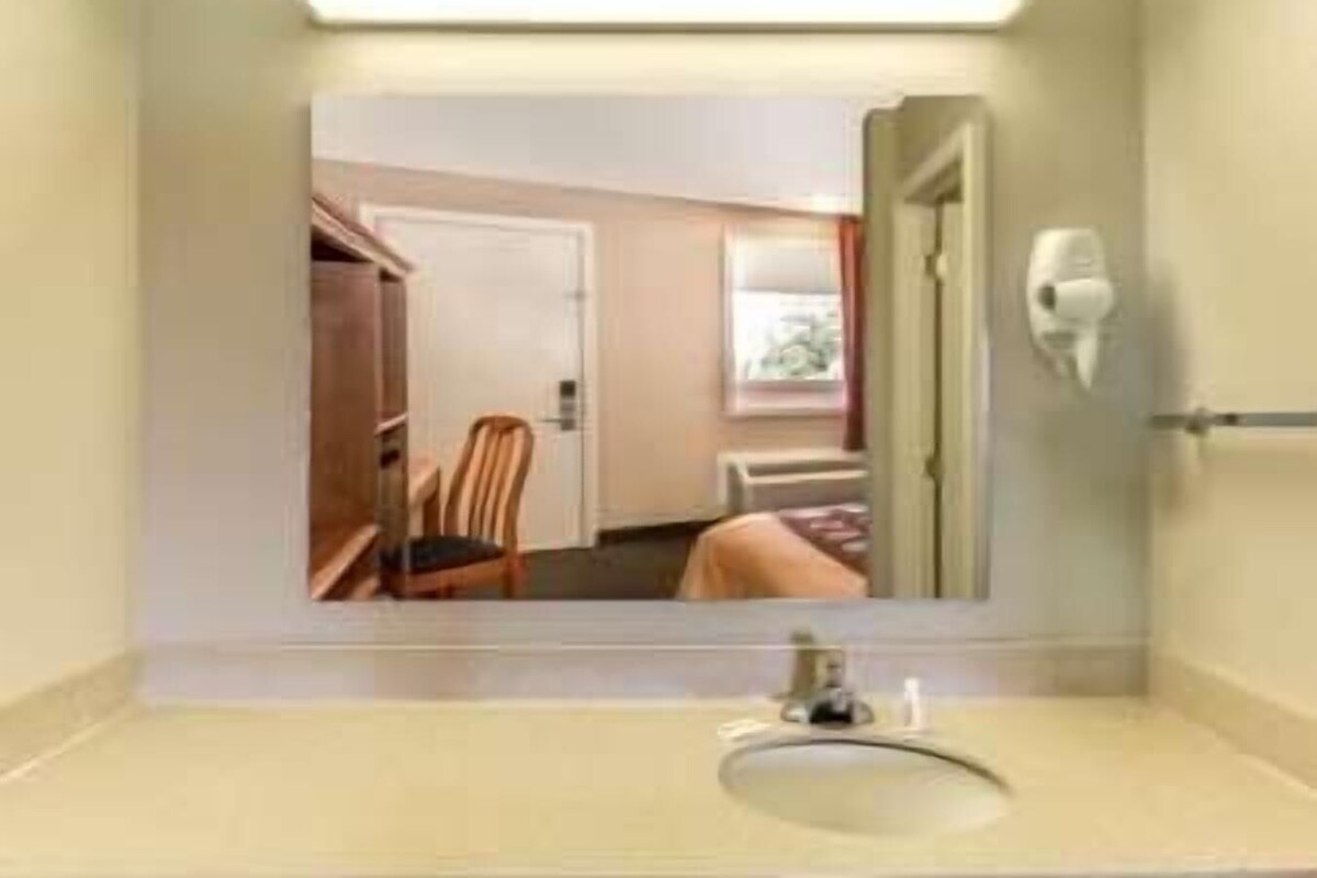 Casa de banho com lavatório, espelho e vista para um quarto através do espelho.