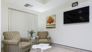 A room with two striped armchairs, a white table, a painting of a tree, a clock, and a TV on the wall. - Super 8 by Wyndham Petersburg (Petersburg)