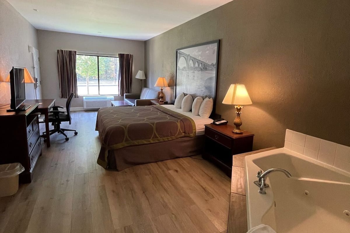 A hotel room with a bed, desk, chair, lamp, and a large window.
