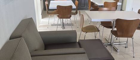 A modern interior with a sofa, dining tables, and a kitchen area.