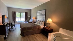 A hotel room with a bed, a desk with a chair, a desk lamp, a large window with curtains, a painting on the wall, and a bathtub. - Super 8 by Wyndham Petersburg (Petersburg)