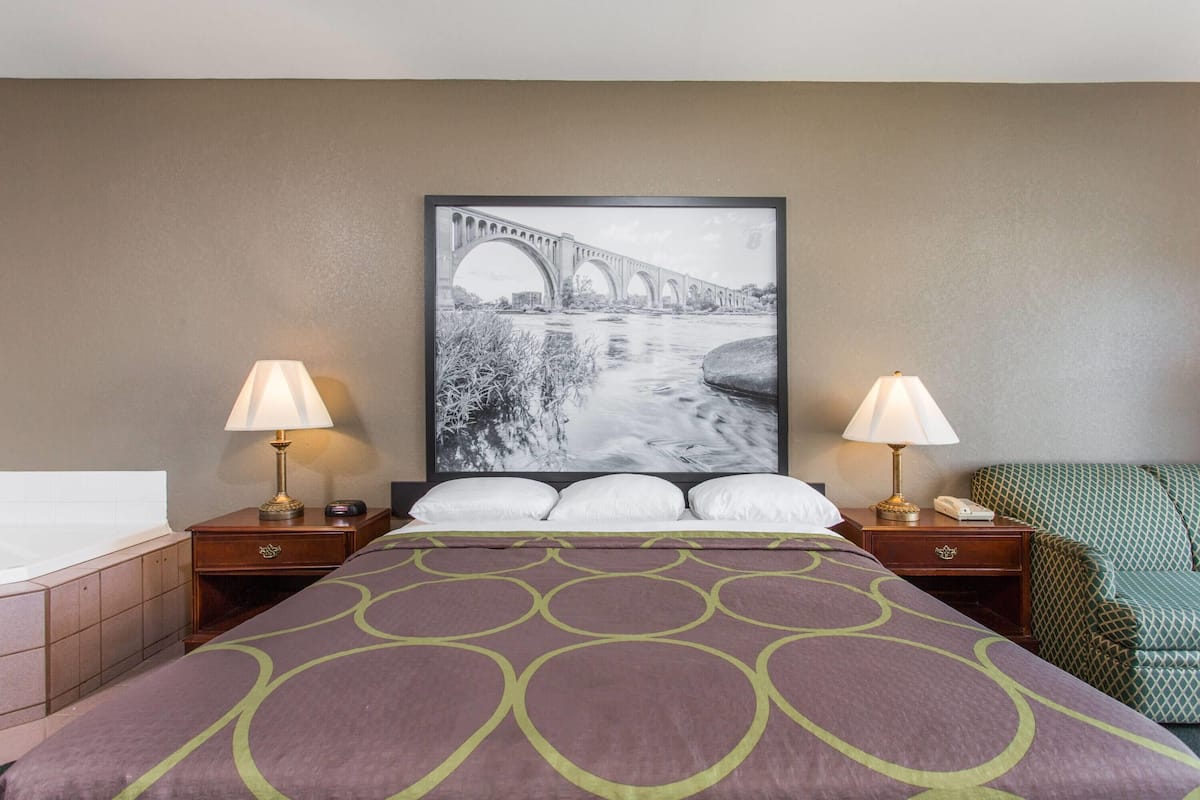 A hotel room with a large bed, two bedside tables with lamps, a large framed picture of a bridge, and a bathtub.