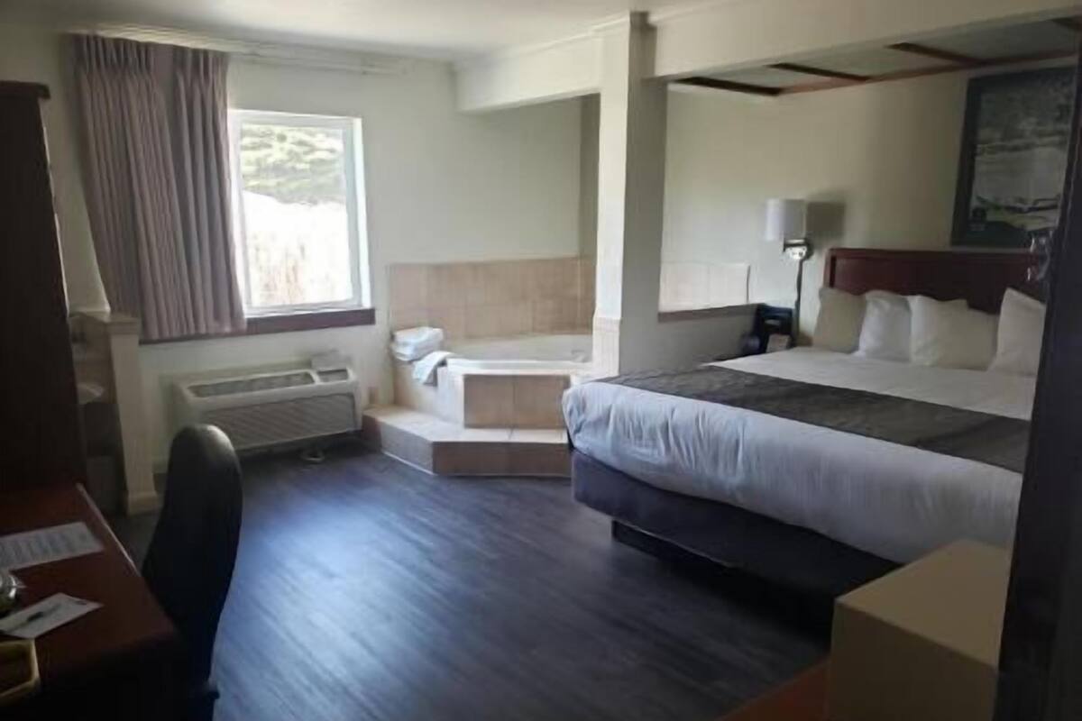 Een hotelkamer met een bed, een bureau, een stoel, een radiator en een raam met gordijnen.