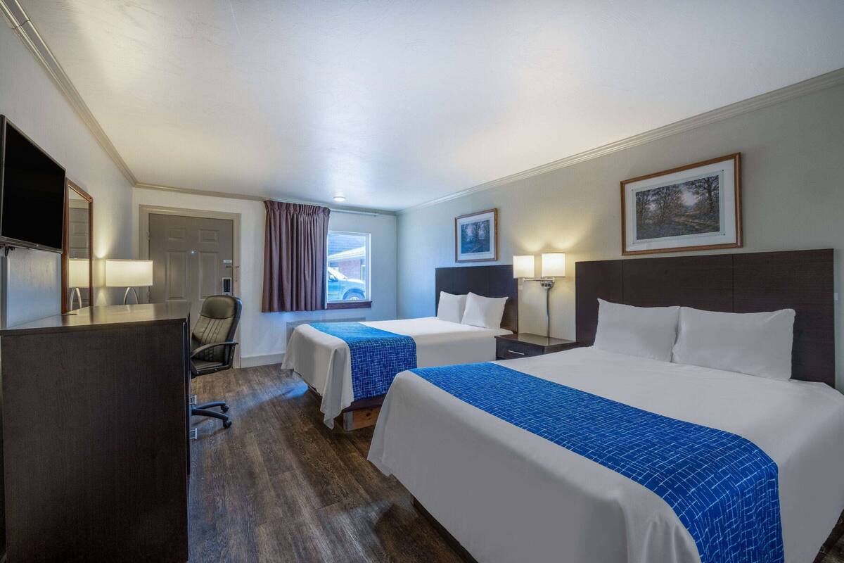 Een hotelkamer met twee bedden, een bureau met stoel, een televisie en een raam met gordijnen.