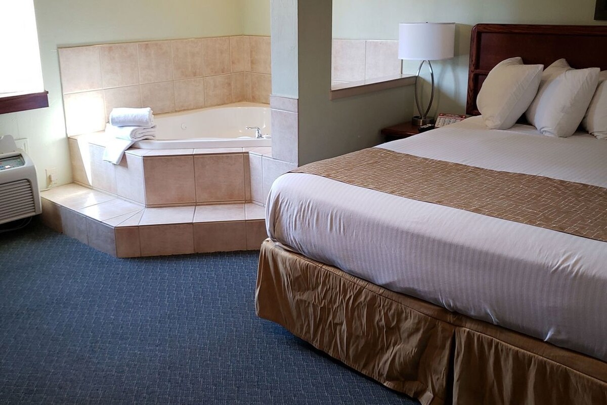 A hotel room with a bed, a small sitting area, a bathtub, and a window.