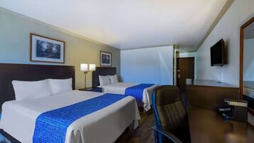 Ein Hotelzimmer mit zwei Betten, einem Schreibtisch, einem Sessel, einem Fernseher und gerahmten Bildern an der Wand.