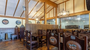 A restaurant interior with wooden furniture, high ceilings, and a view of the city through large windows. - Travelodge by Wyndham Livingston Yellowstone (Livingston)