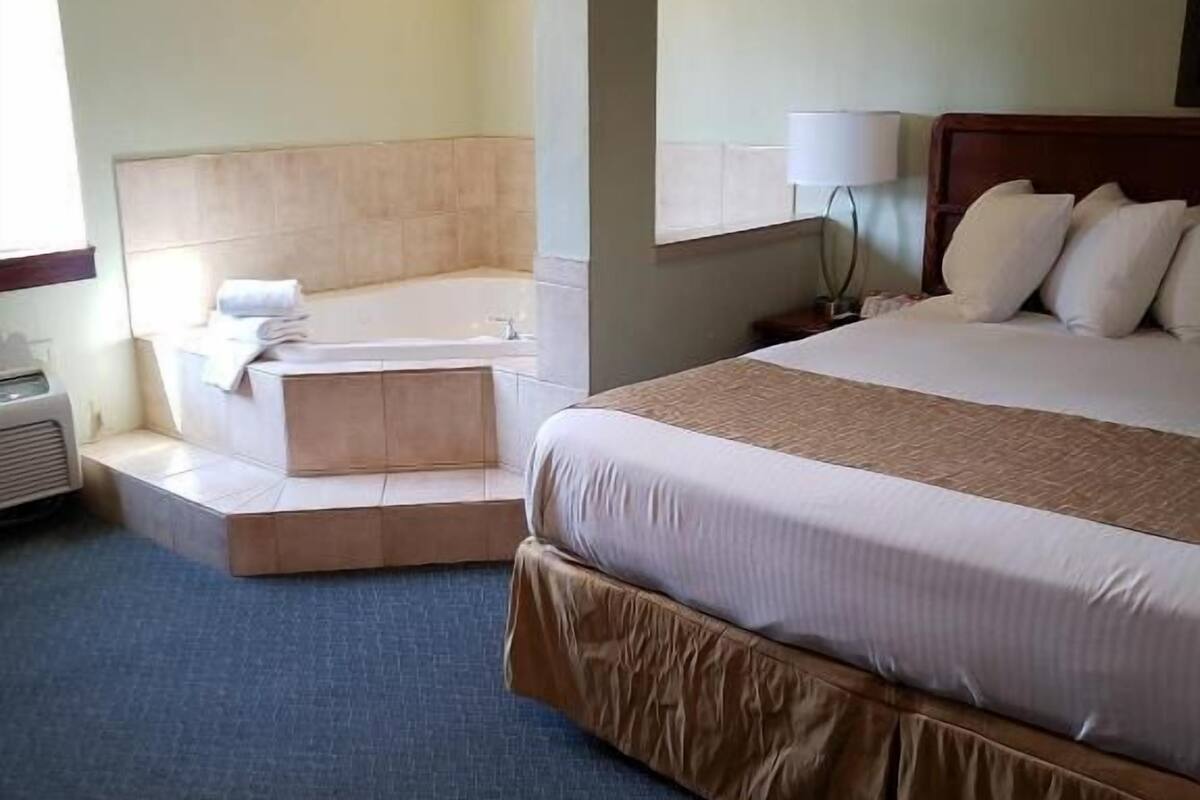 Een hotelkamer met een bed, een zithoek en een badkuip, plus een grote spiegel.