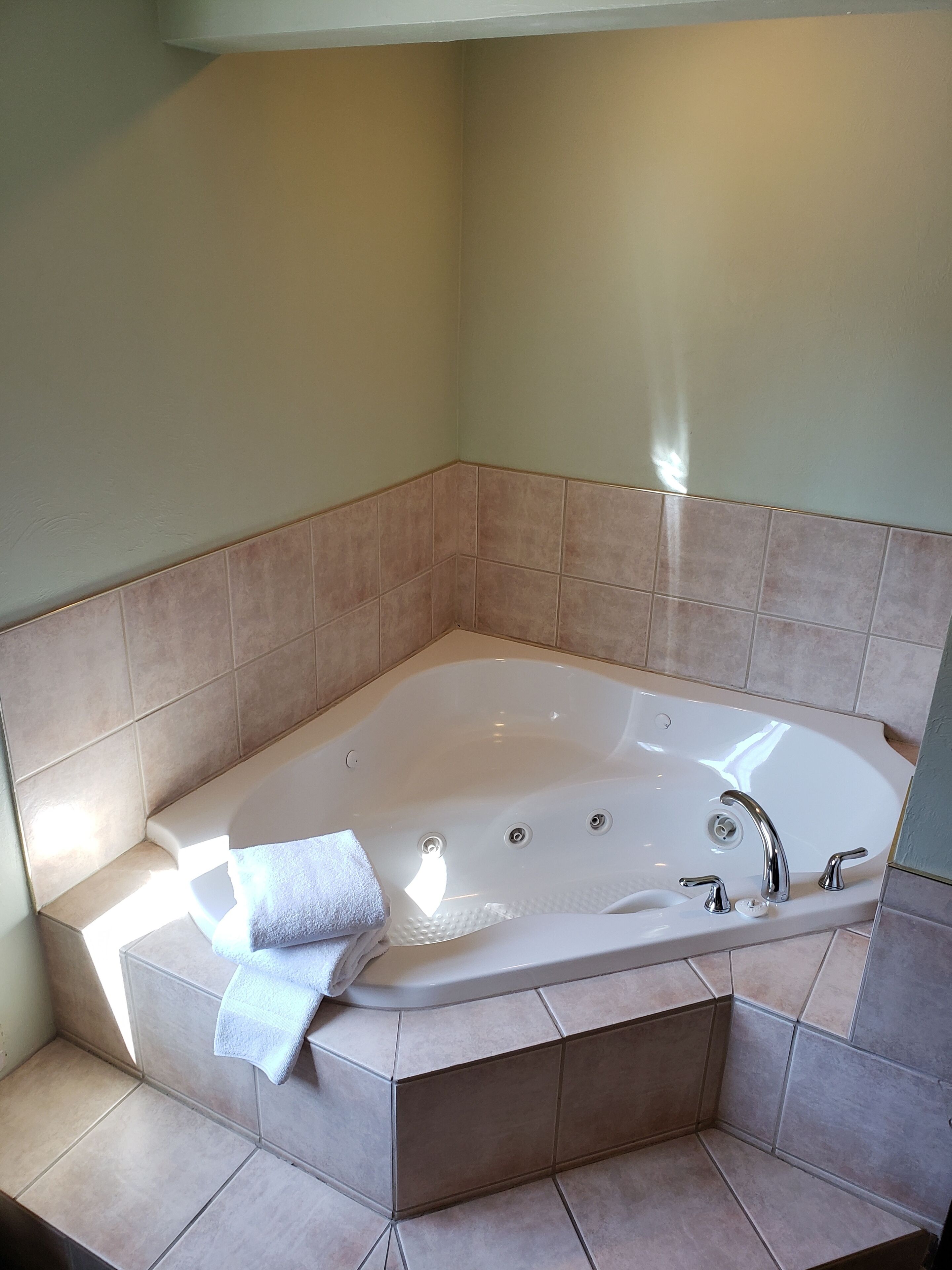 Ein Badezimmer im Eckbereich mit einer freistehenden Badewanne, einem Handtuch und beigen Fliesen.