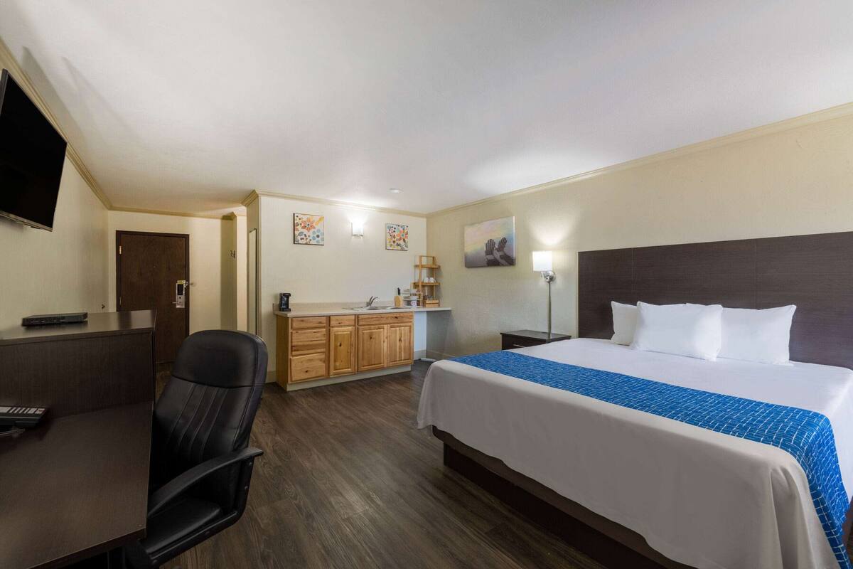 Una habitación de hotel con cama, escritorio, silla, televisión y kitchenette.
