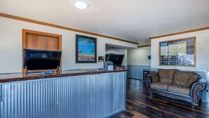 A reception area with a wooden desk, a flat-screen TV, a couch, and framed maps on the walls. - Travelodge by Wyndham Livingston Yellowstone (Livingston)