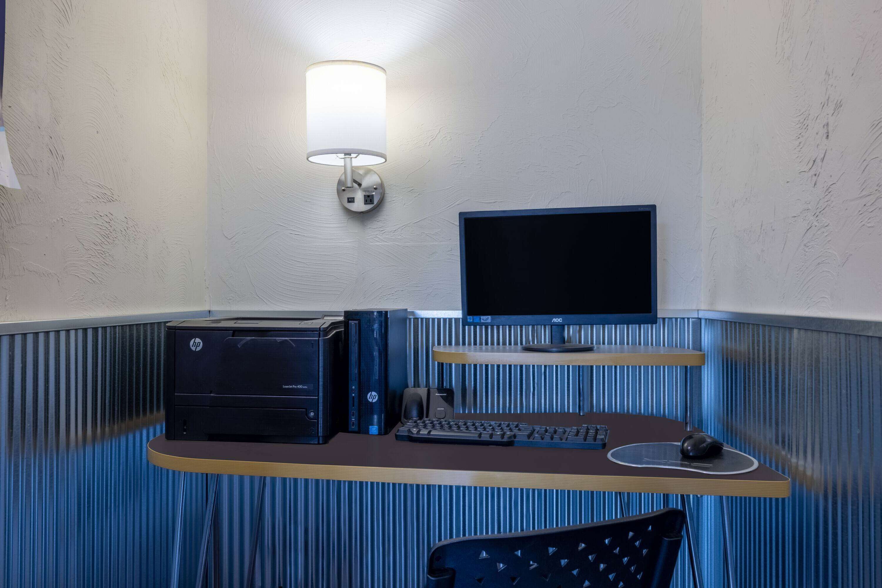 A compact office space with a desktop computer, monitor, keyboard, and mouse on a desk. A printer and speaker are also visible.