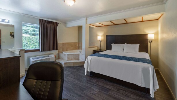 A hotel room with a bed, desk, chair, and a view of greenery outside. - Travelodge by Wyndham Livingston Yellowstone (Livingston)