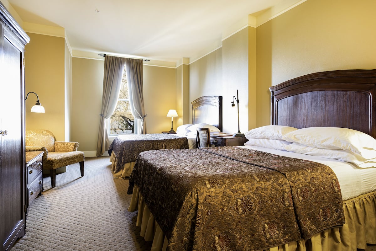Une chambre d’hôtel avec deux lits, un bureau, une chaise et une fenêtre avec des rideaux.