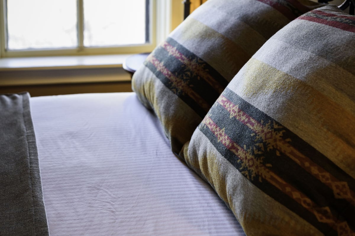 Un lit avec un oreiller à motifs, une lampe de chevet et une fenêtre avec des rideaux.