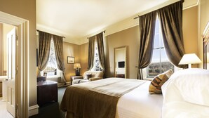 Ein Hotelzimmer mit einem großen Bett, einem Schreibtisch, einem Sessel, einem Fenster mit Vorhängen und Blick ins Freie.