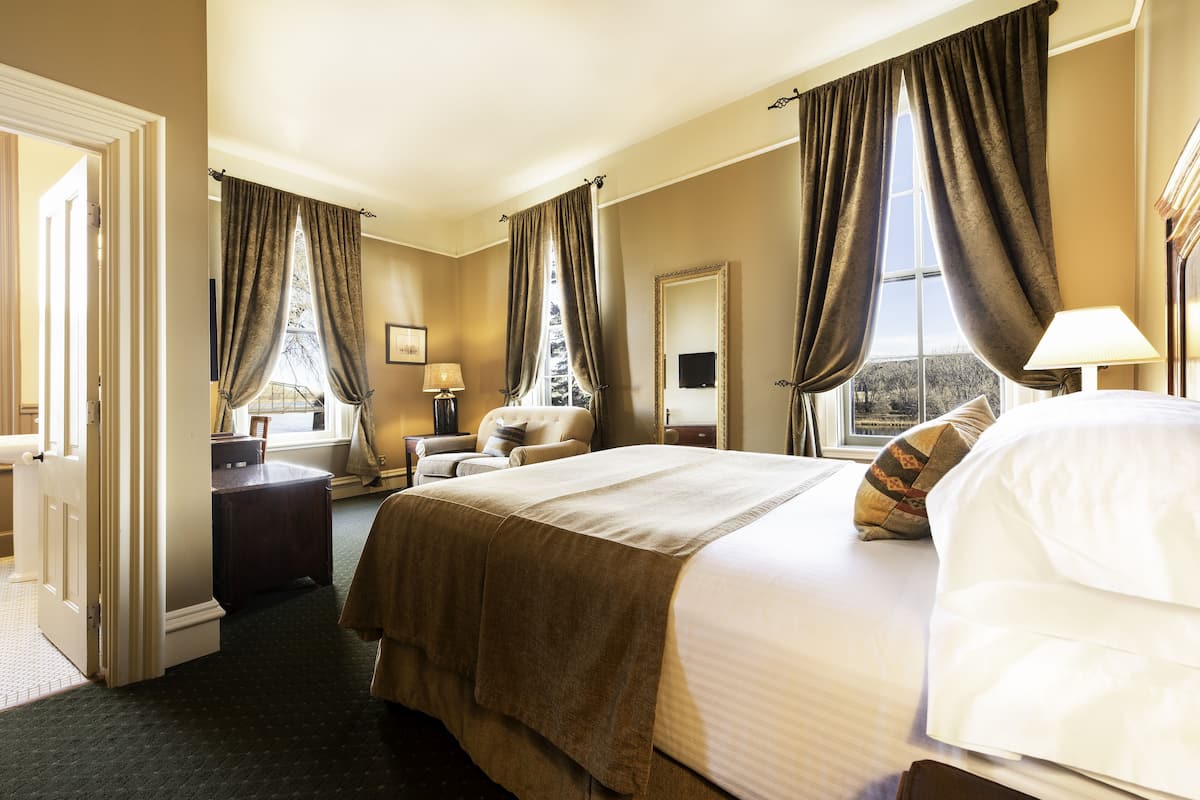 Une chambre d’hôtel avec un grand lit, un bureau, une chaise, une fenêtre avec des rideaux et une vue sur l’extérieur.