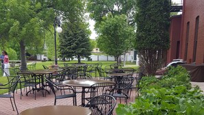Terrasse mit Tischen und Stühlen, umgeben von Grünflächen und einem Pflasterweg.