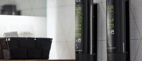 A bathroom with a wooden shelf holding a black basket, and two black bottles of Fair Trade Body Lotion on the wall.