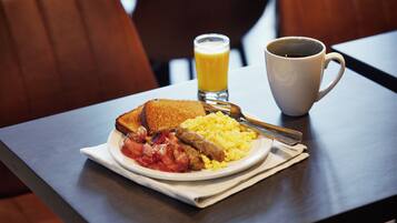 A breakfast plate with toast, bacon, scrambled eggs, and a glass of orange juice on a table.