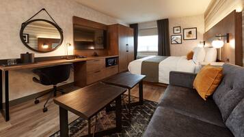 Ein modernes Hotelzimmer mit einem Holztisch, einem bequemen Sofa, einem Bett mit weißer Bettwäsche, einem großen Spiegel und Blick auf die Stadtlandschaft.
