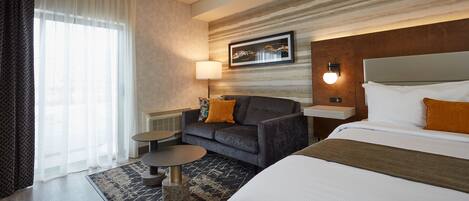 A hotel room with a bed, a sofa, a small table, a lamp, and a picture on the wall.