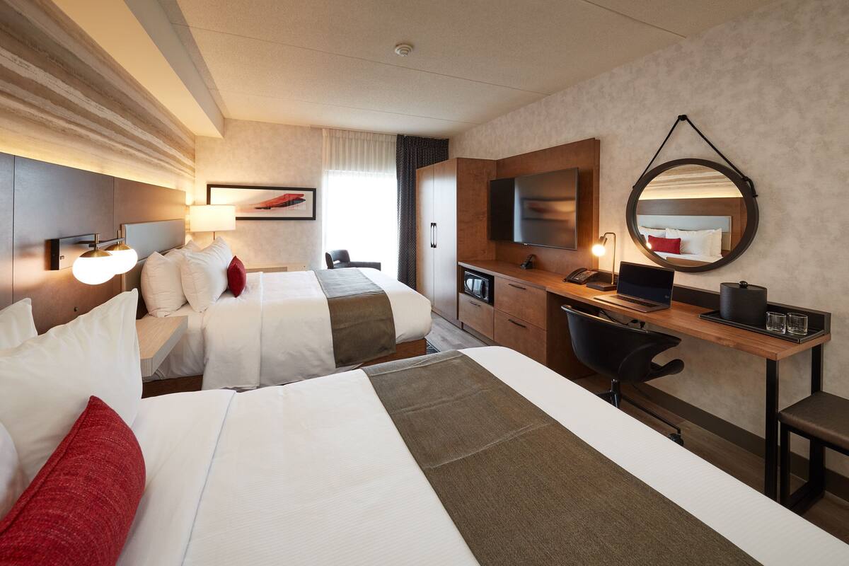 A hotel room with two beds, a desk with a laptop, a mirror, and a TV.