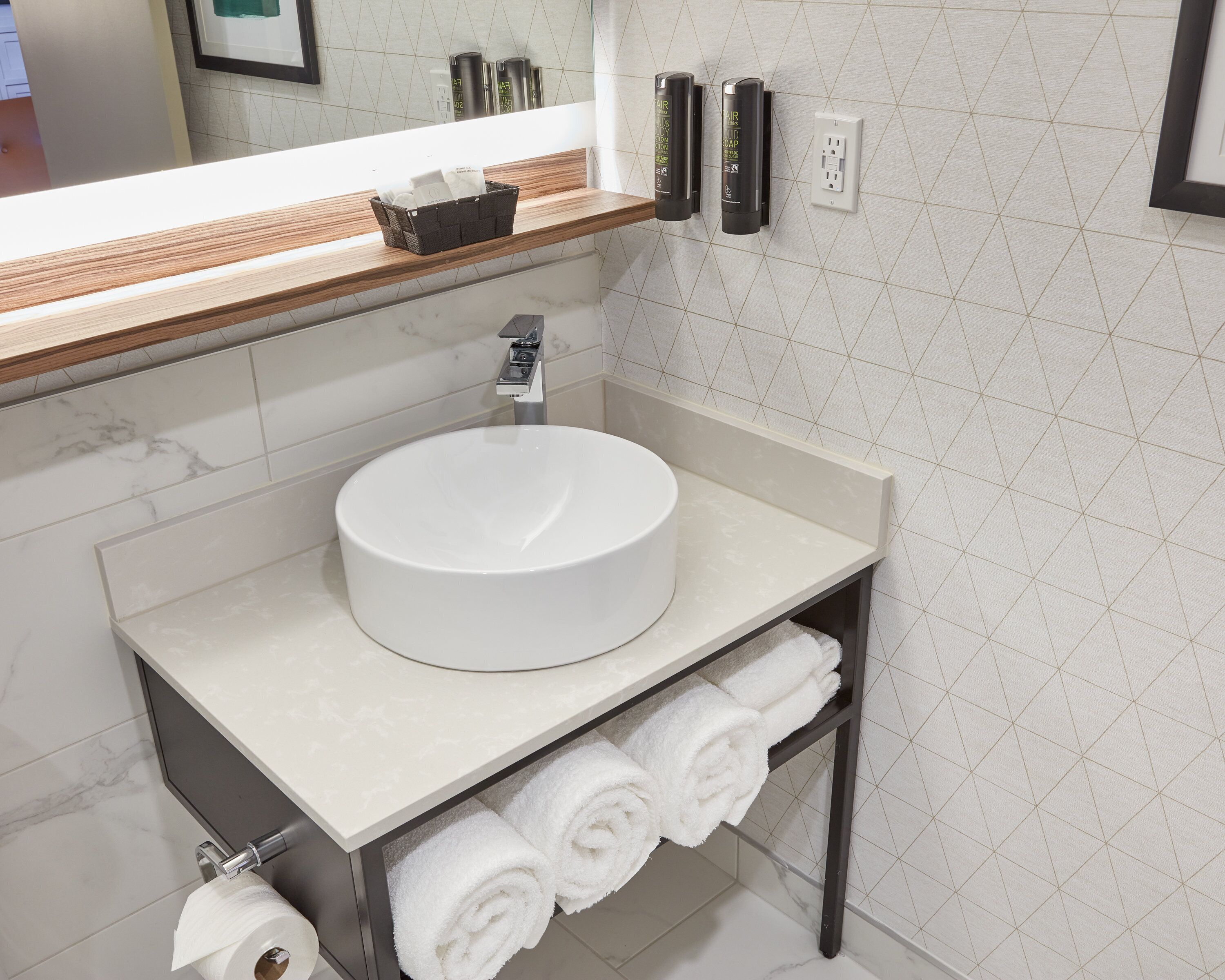 A bathroom with a round sink, a mirror, a towel rack, and toiletries on the wall.