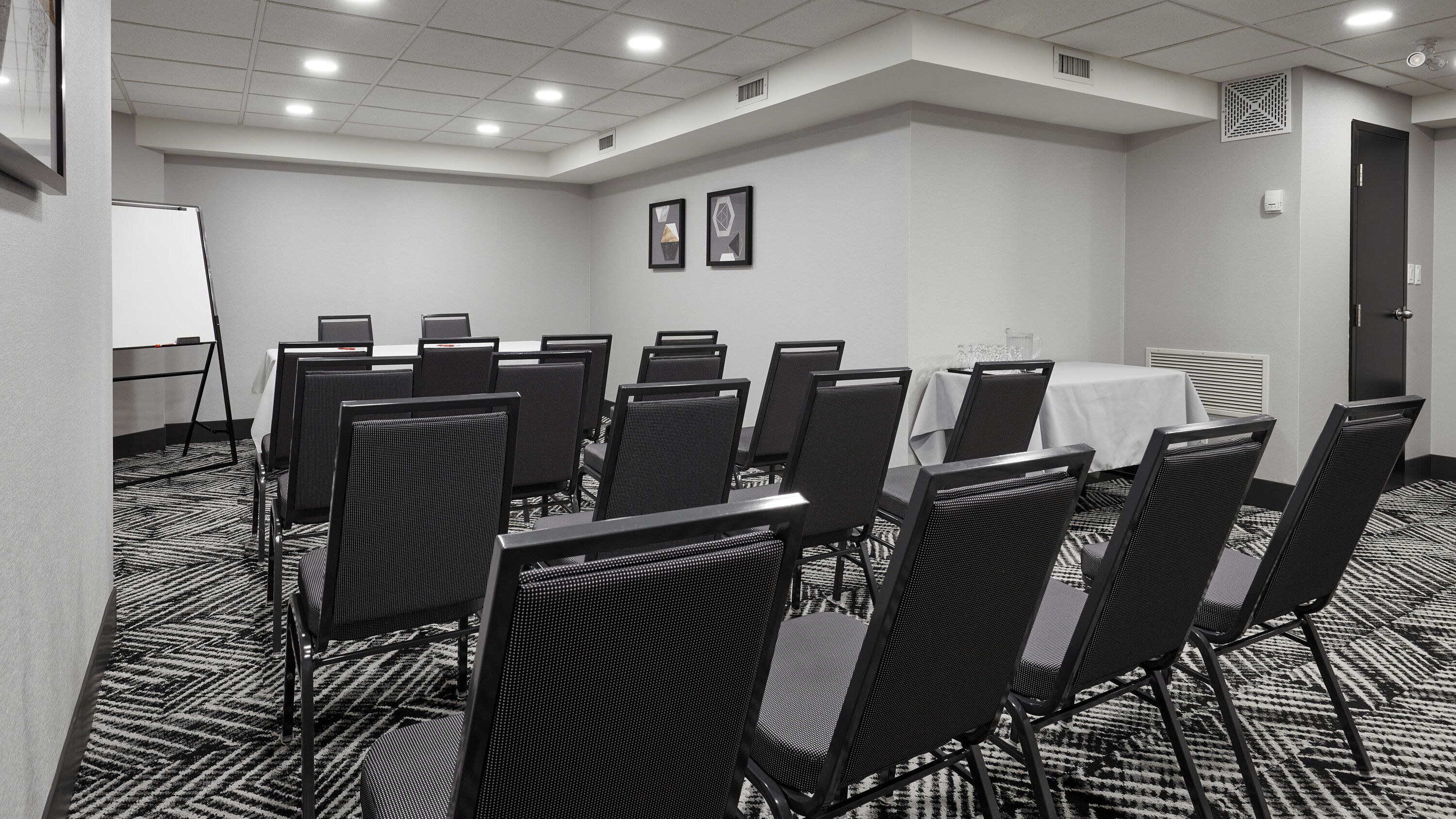 Una sala de conferencias con una mesa blanca, sillas negras y una pizarra.