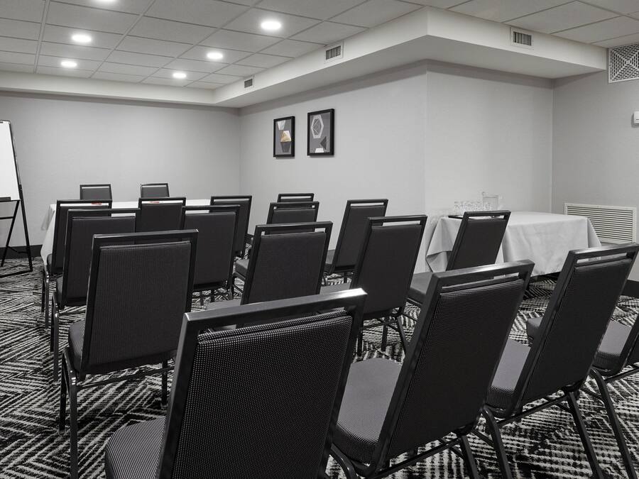 Una sala de conferencias con una mesa blanca, sillas negras y una pizarra.