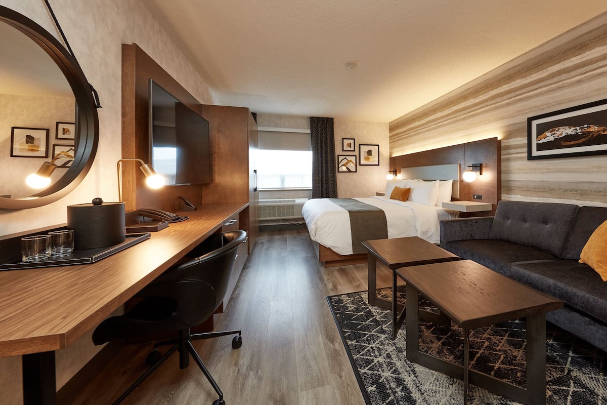 A modern hotel room with a wooden desk, a sofa, a bed, and a large mirror.