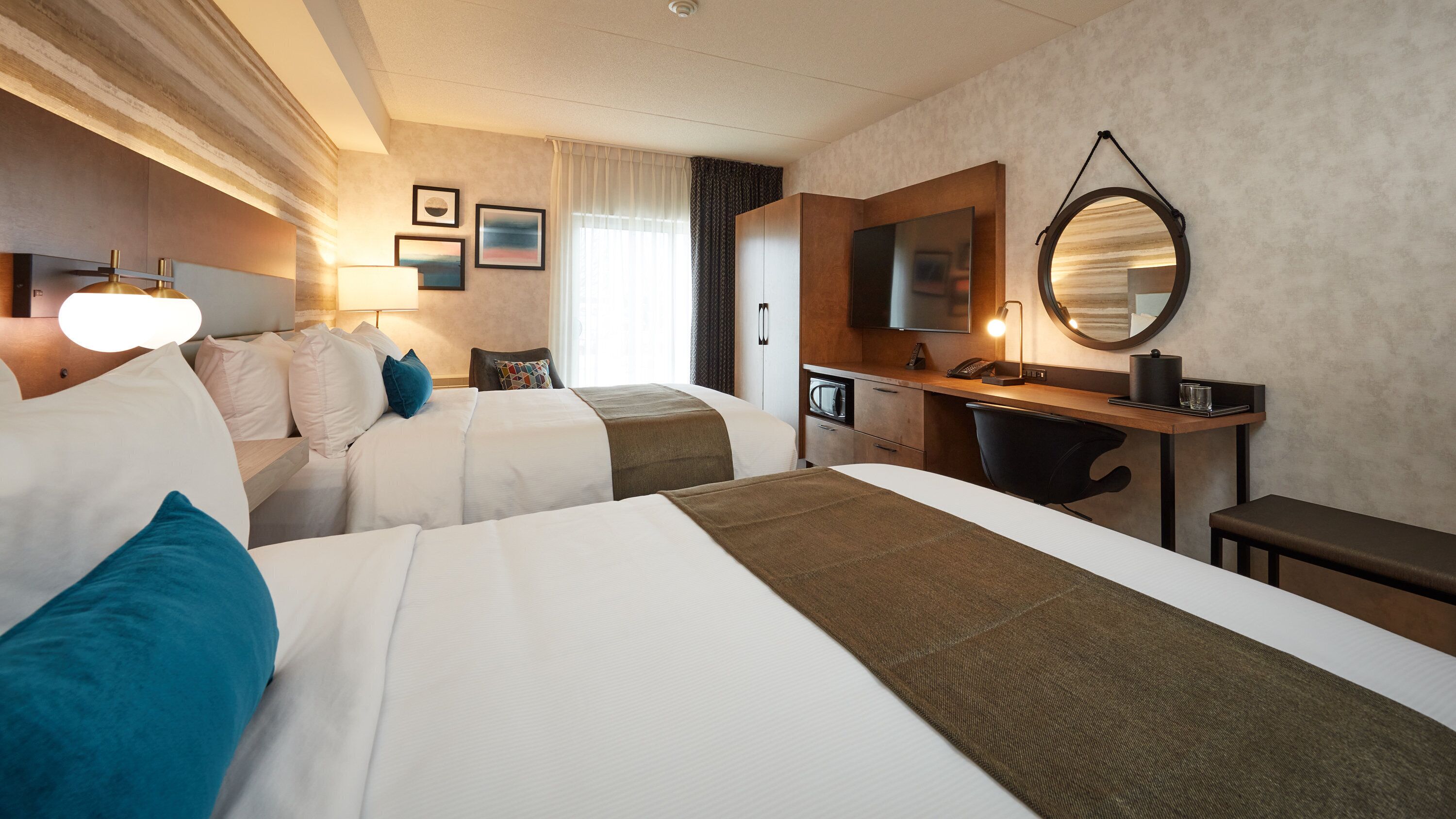 Quarto de hotel com duas camas, uma mesa, uma televisão e um espelho.