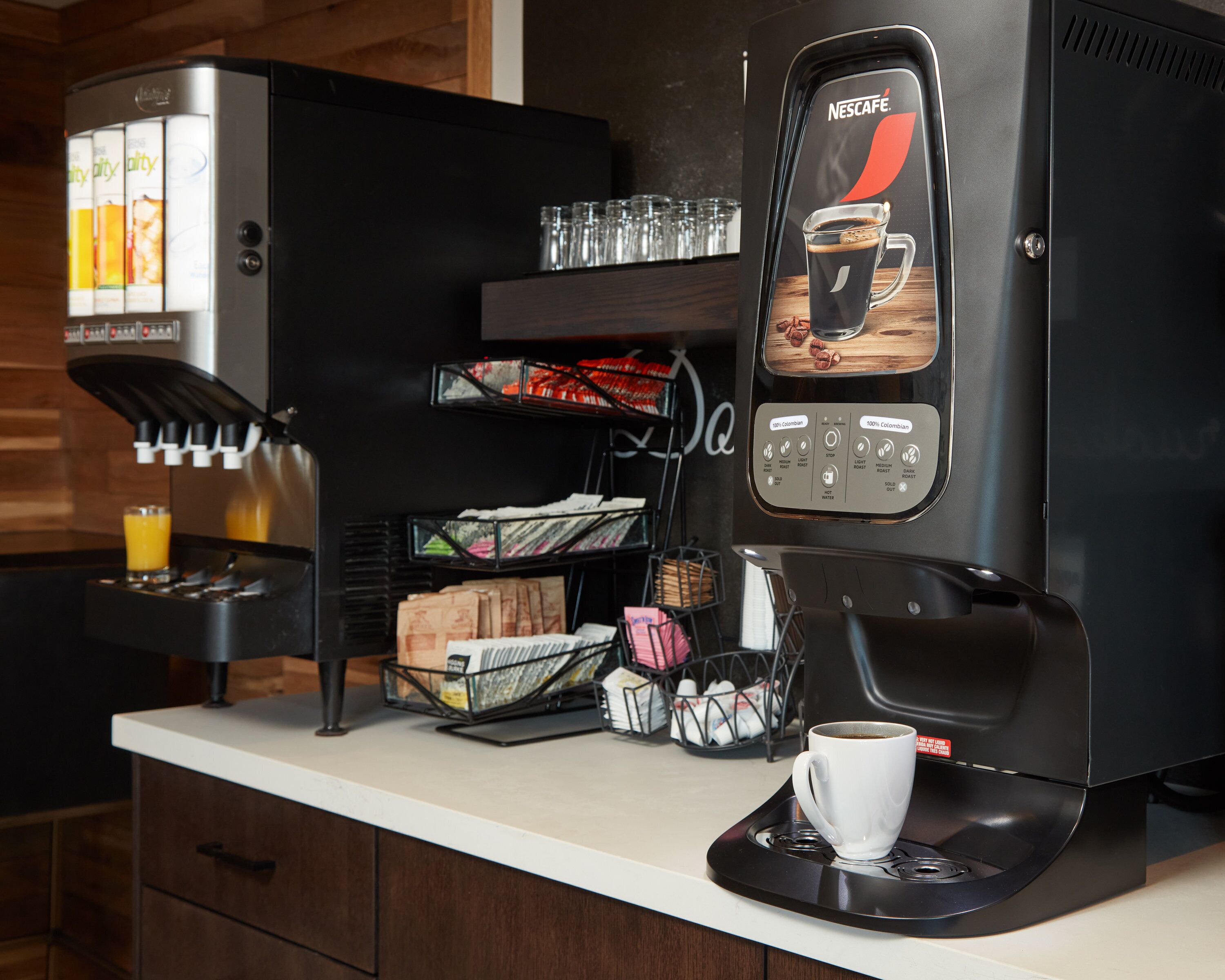 A coffee machine with a touchscreen interface, a coffee cup on a tray, and a juice dispenser.