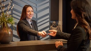 A reception desk with a modern design, a vase with a plant, and a statue in the background.