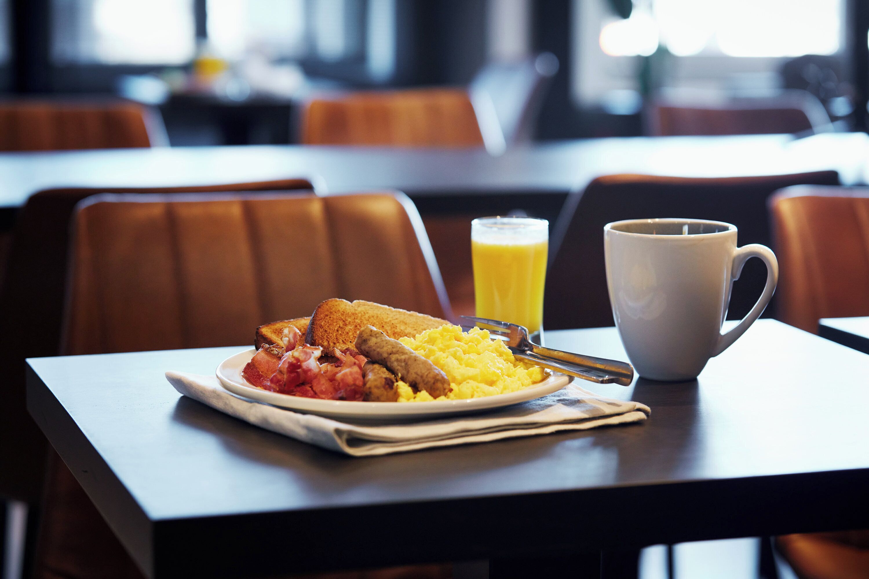 A breakfast setting with toast, scrambled eggs, bacon, and a glass of orange juice on a table.