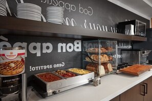 A buffet area with various food options, including waffles, meats, and cheeses, displayed in a buffet station with a chalkboard sign above.