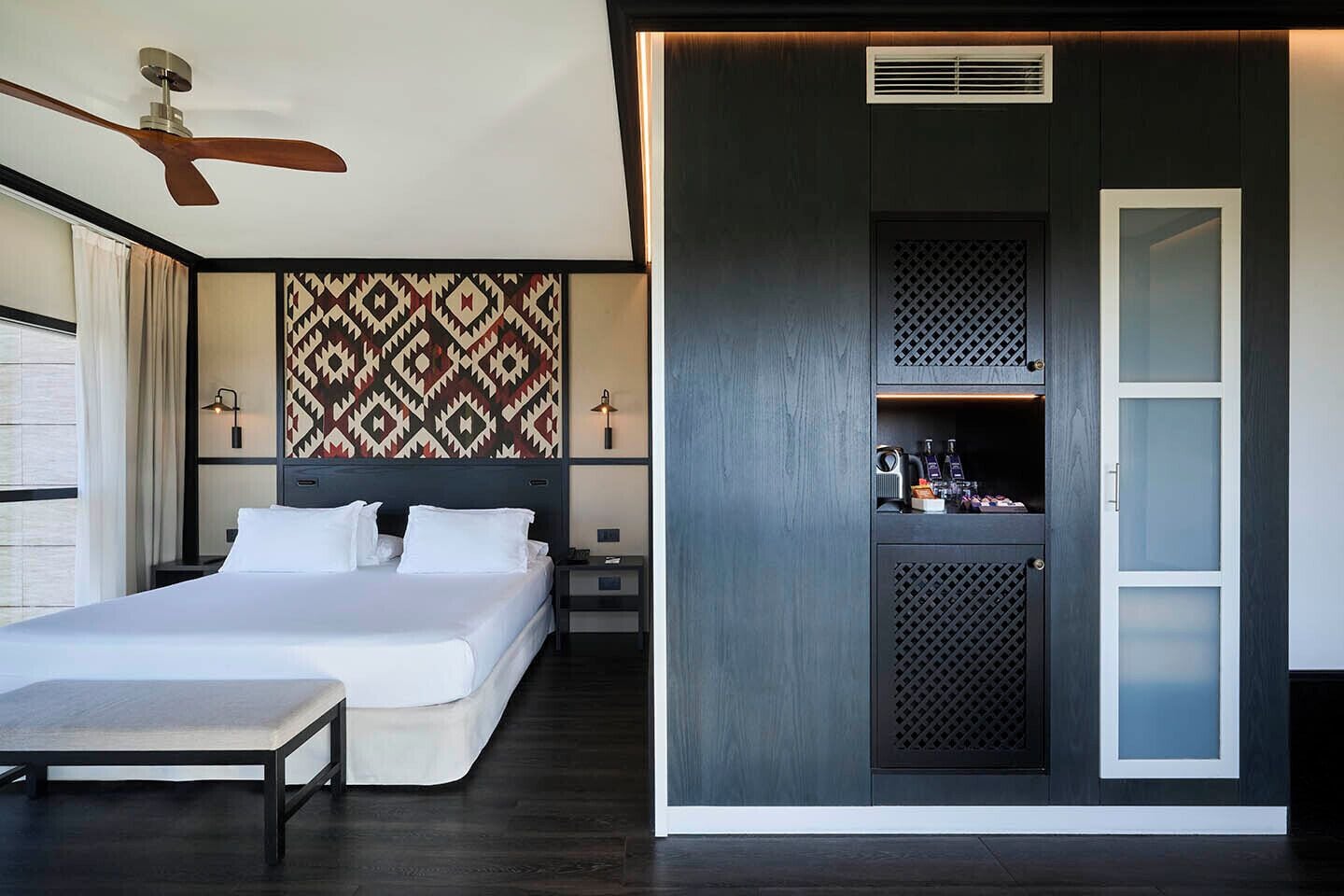 Une chambre d’hôtel moderne équipée d’un lit, de tables de chevet, d’un bureau, d’une armoire et d’un ventilateur de plafond.