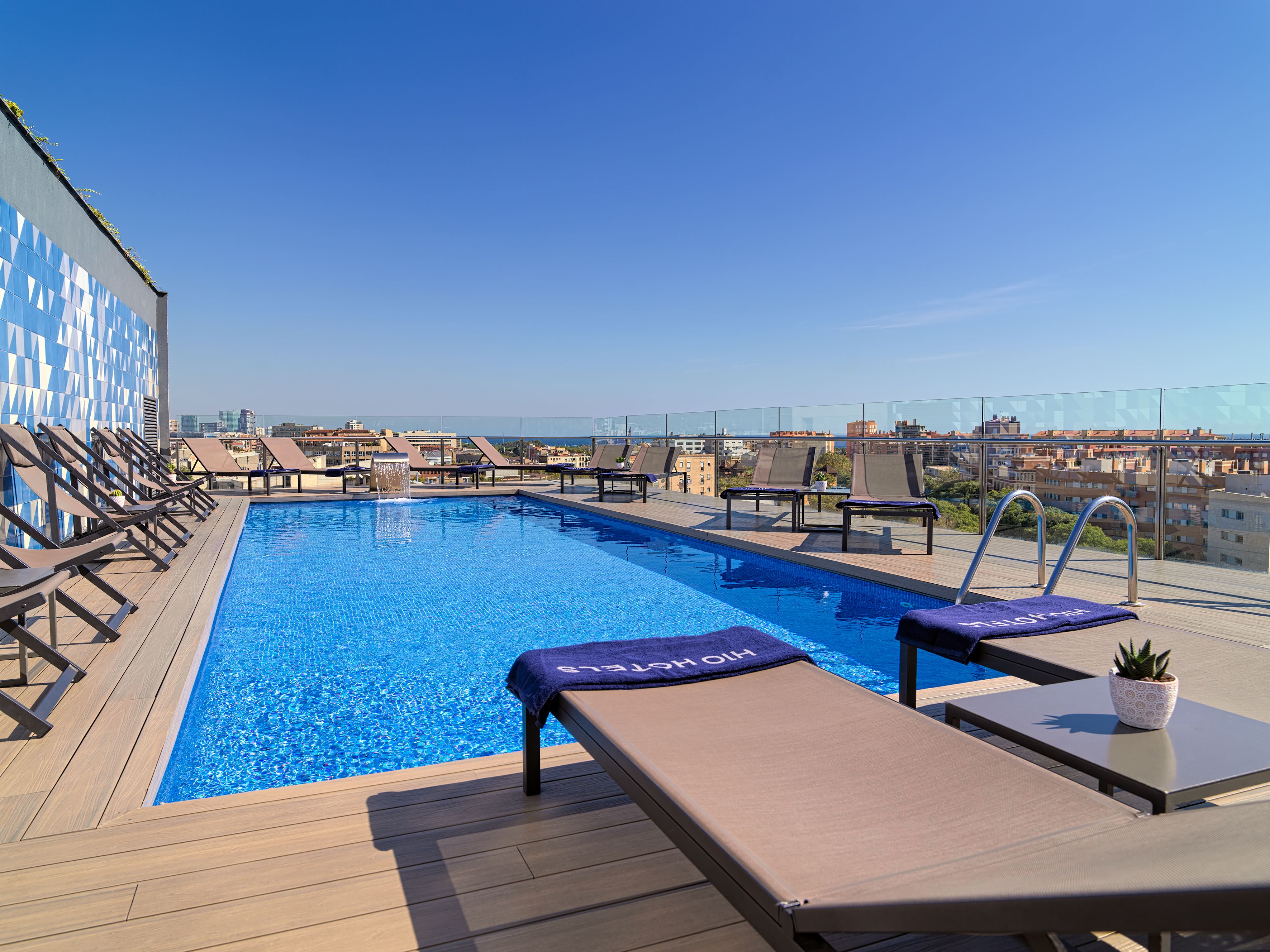 A rooftop pool with lounge chairs and a city view.