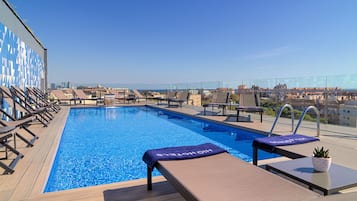 A rooftop pool with lounge chairs and a city view.