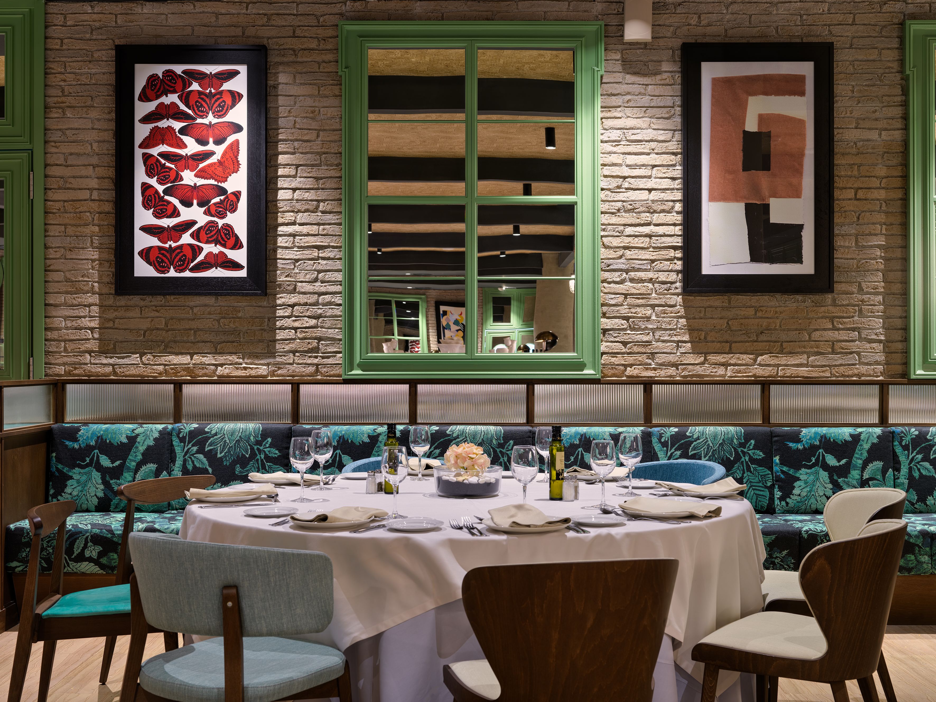 Un restaurante con pared de ladrillo, obras de arte enmarcadas, una ventana verde y una mesa lista para comer.
