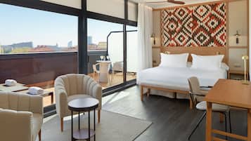 Een hotelkamer met een groot bed, een plafondventilator, een eettafel en een balkon met uitzicht op de stad.