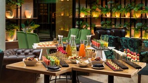 Un comedor con varias mesas, sillas tapizadas de verde y una pared decorada con plantas en macetas.