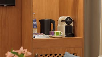 Habitación de hotel con un mueble de madera que contiene una tetera, cafetera y tazas. Hay un televisor montado en la pared y un florero con flores sobre la mesa.