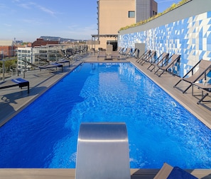 A rooftop swimming pool with lounge chairs and a view of the city.