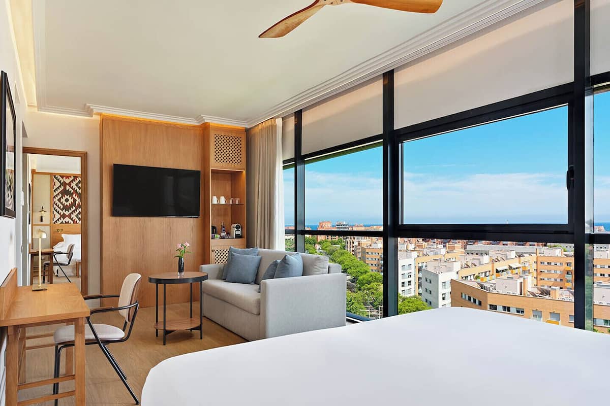 Une chambre d’hôtel moderne dotée d’un grand lit, d’un canapé, d’un bureau avec une chaise, d’une télévision et offrant une vue sur la ville.