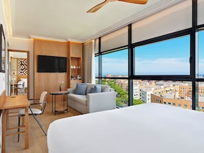 Ett modernt hotellrum med en stor säng, en soffa, ett skrivbord med stol, en TV och utsikt över staden.