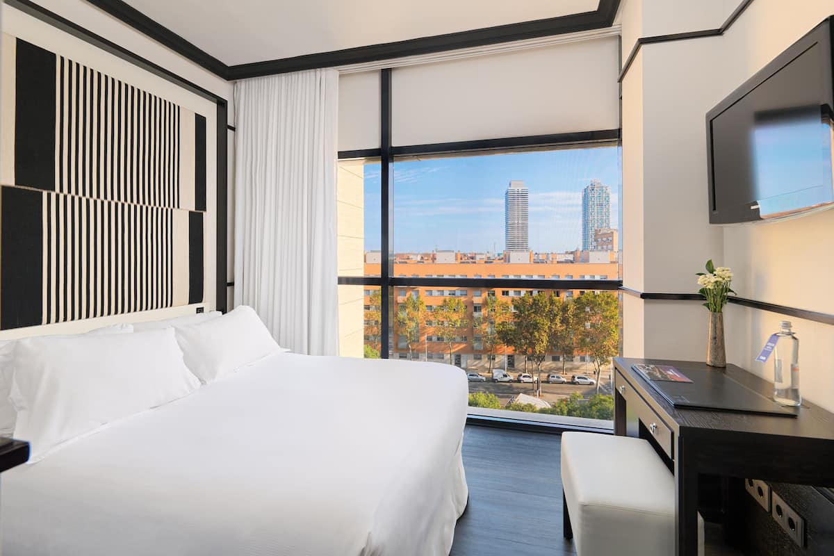 Ein modernes Hotelzimmer mit einem großen Bett, einem Schreibtisch und Blick auf die Stadt.