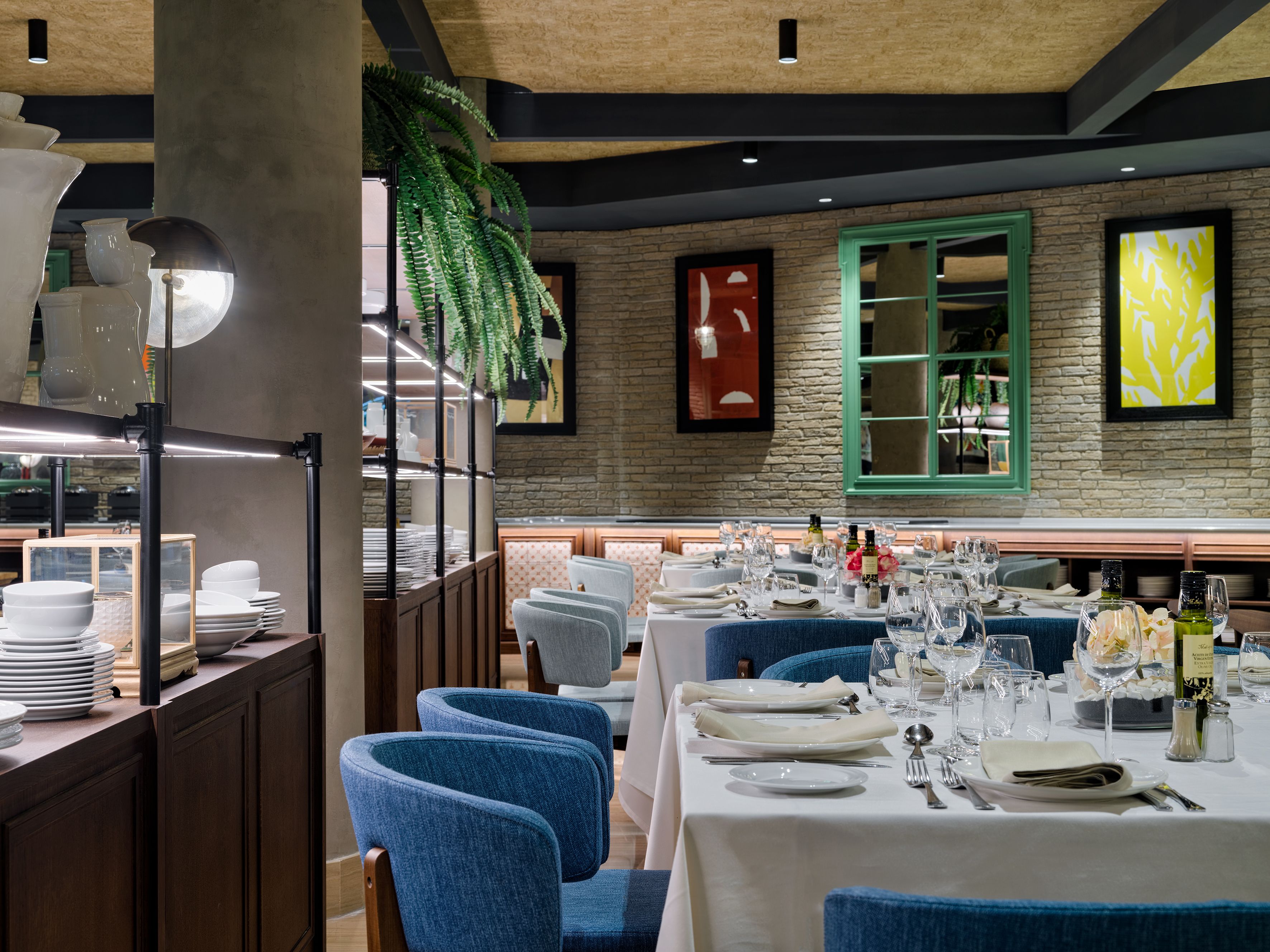 A restaurant with a rustic stone wall, green window, and blue upholstered chairs.