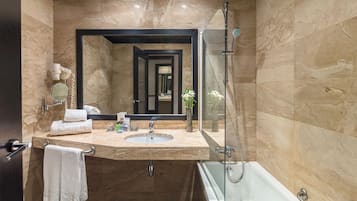 A modern bathroom with a marble vanity, a large mirror, a glass-enclosed shower, and a bathtub.